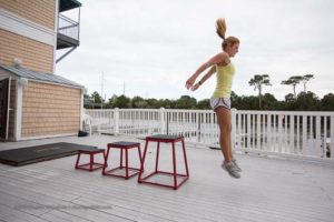 woman box jumping off of gym deck