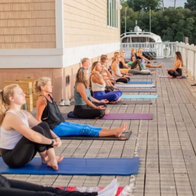 a row of gym members sit on yoga mats on the back deck t inlet fitness in virginia beach