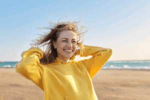 Woman in yellow sweatshirt looking happy and energetic on the beach.